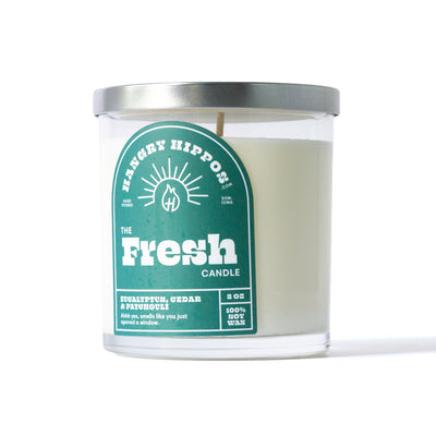 Candle with silver lid. Clear jar with green label "The Fresh Candle"